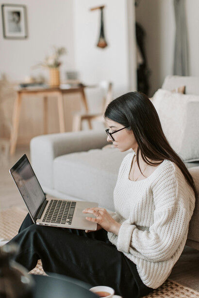 A woman deeply engaged in writing on her laptop, seated on the floor at home