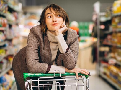 Una donna si appoggia a un carrello della spesa in un corridoio di supermercato, con un'espressione pensierosa