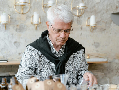 Seated at a table, a figure examines various perfume bottles
