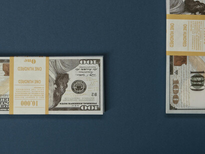 A backdrop of hundreds of dollar bills contrasts with the subdued demeanor of a modern worker