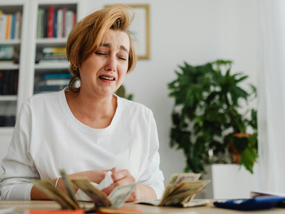 A woman counts money and pays household bills at home, visibly distressed by financial pressure