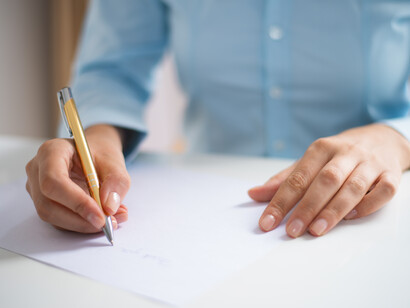 Una persona scrive con una penna dorata su un foglio di carta bianco