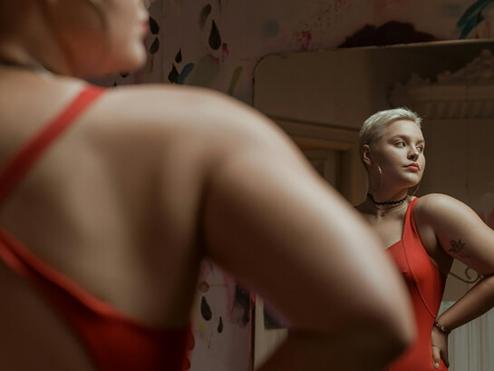 A girl looking at her reflection at the mirror in red dress