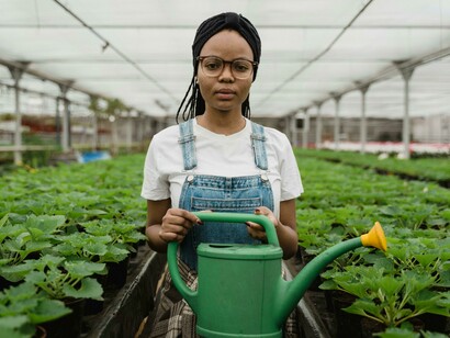 Woman holding a green watering can and looking at the camera, representing the agricultural industry, agricultural work, agriculture, and agronomy