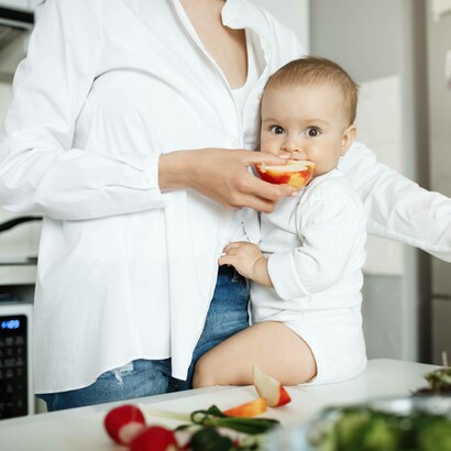 Mamma che porge al bambino una fetta di mela: "Una dieta varia ed equilibrata, ricca di frutta, verdura, proteine di qualità e grassi sani, è essenziale per garantire uno sviluppo ottimale"