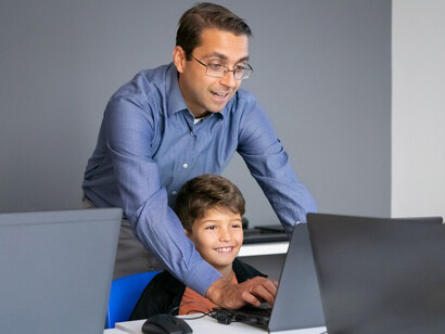 Teacher in glasses explaining lesson to boy and standing behind him