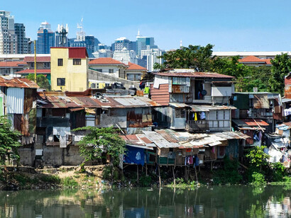 A contrast of poverty and wealth: riverside slums set against the backdrop of towering city buildings