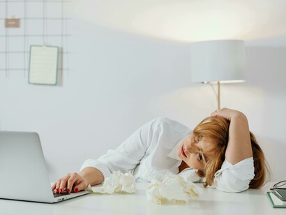 A short-haired woman leans on a table, surrounded by screens, expressing information overload and mental fatigue