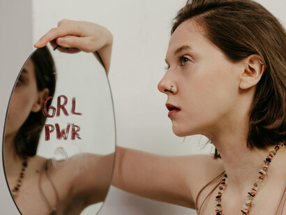 A young woman holding a mirror with a phrase written with lipstick