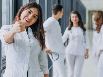A female doctor smiling and giving a thumbs-up in the hospital corridor, representing compassion and ethical medical practice