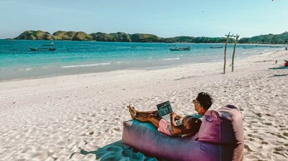 A man sitting on a bean bag on the beach, working on his laptop in Lombok