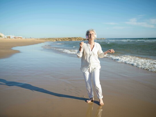 Mulher desfruta de música enquanto caminha na praia. Não importa onde você está. Não importa o que já viveu ou deixou de viver. Sempre há espaço para um novo capítulo. Pense nos anos que já passaram. Quantas vezes você se reinventou sem perceber? Talvez tenha mudado de emprego, de cidade, de relacionamento, de direção. A vida é feita de recomeços, mesmo que a gente não os chame assim