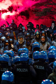 A heated standoff unfolds between riot police and protesters, the air thick with the anticipation of conflict and the weight of personal struggles behind every helmet