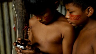 Crianças indígenas manuseiam smartphone. Estudiosos como José Augusto Pádua têm trabalhado na interseção entre história ambiental e social, examinando como as mudanças ambientais influenciaram as estruturas sociais e as experiências individuais ao longo do tempo