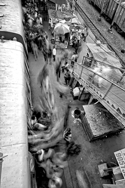 A blurred crowd rushes past a train station—capturing the relentless motion and disorientation of life in an accelerated society