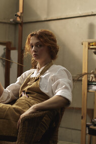 A woman, dressed in a white long-sleeved blouse and adorned with a brown apron