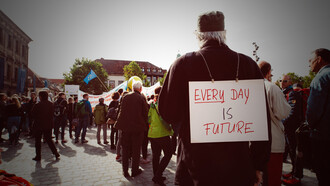 Man holding a banner reading “Every Day Is Future” during a protest