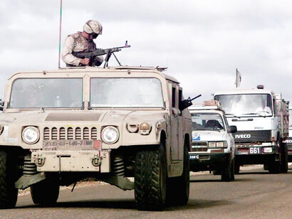 A convoy moves along the road from Mogadishu to Baidoa, led by a desert-camouflaged M998 HMMWV from the U.S. Marines’ 2nd Platoon, “C” Company, 3rd Light Assault Infantry Battalion. A Marine mans an M60 machine gun from the turret as United Nations trucks carrying food supplies for Somali feeding centers follow behind in support of Operation Restore Hope