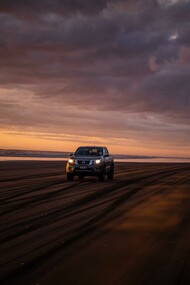 A car driving alone on a beach at sunset