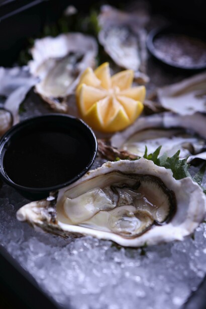 A bed of ice cradles freshly shucked oysters, garnished with lemon wedges 