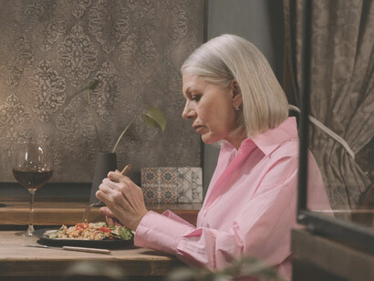 A woman dressed in pink long sleeves sits alone at dinner, capturing the essence of isolation