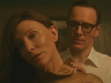 In a warm, amber-lit room, George (Michael Fassbender) tenderly adjusts Kathryn’s (Cate Blanchett) dress, a moment of vulnerability in their tightly wound spy marriage