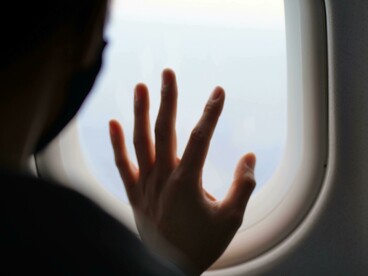 From an airplane window, a traveler points at the vast sky beyond the clouds