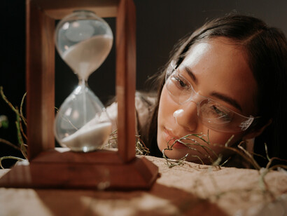 A woman looking closely at an hourglass, representing the shift from accepting time to actively influencing it