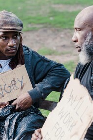 Two men hold signs that indicate poverty