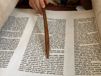 A human hand guides a yad along the Hebrew script