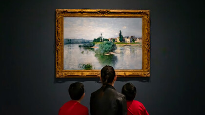 A woman in a black jacket sits on a red sofa with two children inside an art museum
