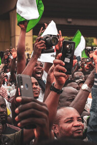 In the heart of Nigeria, amidst waving flags, individuals gather with their phones, showcasing how mobile technology has revolutionized communication, connecting loved ones effortlessly and bridging geographical barriers