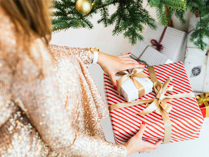 A woman placing Christmas presents beneath a tree, representing the shared ritual of giving for Christmas