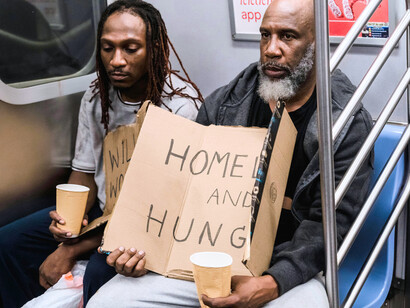 Two people seated in a subway, holding a simple sign that says they are homeless, symbolising how lives are disrupted by eviction