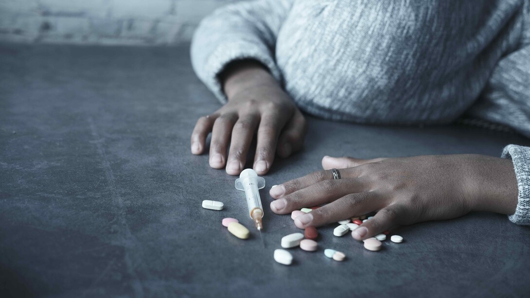 A person unconscious beside pills, a syringe, and other drugs