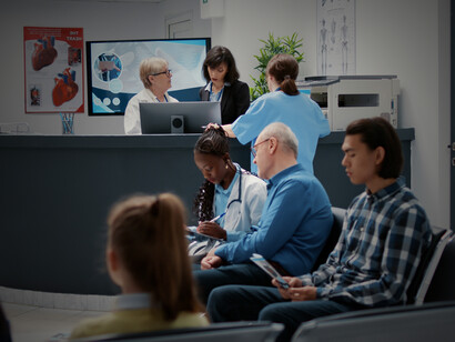 A crowded hospital waiting room near the reception desk, filled with people of all backgrounds waiting for checkups, consultations, or urgent care