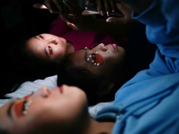 Young women lying on a bed, focused on their phones