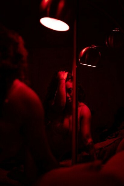 A woman wearing underwear, illuminated by deep red lighting in a dark room