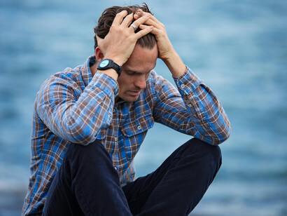 A sad and lonely man in a blue and brown plaid shirt touches his hair in despair