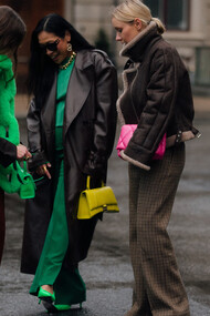 Estilista encontra as amigas enquanto usa um cachecol verde na forma de uma corrente em alusão ao compromisso com a sustentabilidade