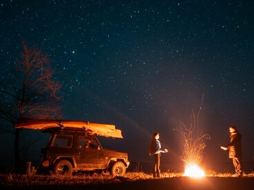 Two travellers standing beside a glowing desert campfire under a star-filled sky, representing the quiet wonder of Saharan nights