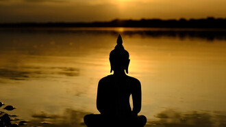 A Buddha statue seated peacefully in front of a calm body of water