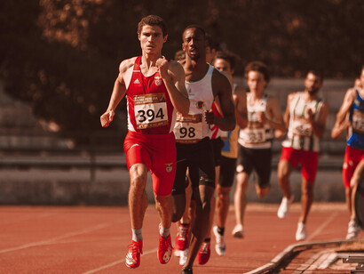 An Olympic athlete in a red tank top sprints with his eyes shut during the race