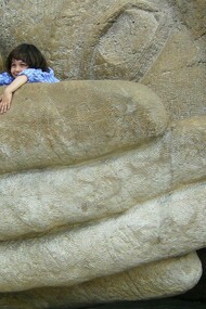 A child sits inside the giant hand of a face statue