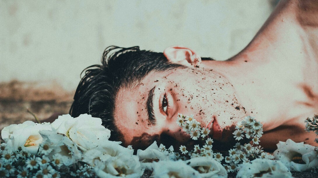 A man lies down next to daisies, looking upset