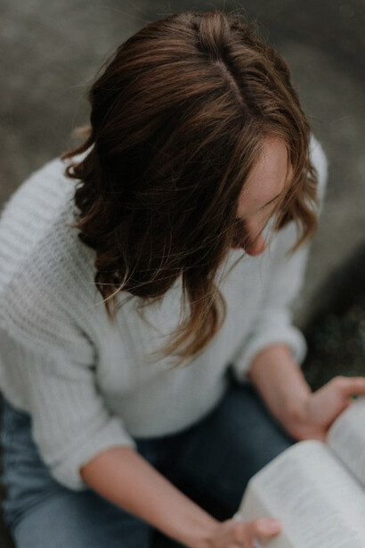 A woman sits on the gray concrete pavement, holding and reading her Bible in a moment of reflection