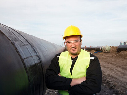 A portrait of an industrial worker standing next to a gas pipeline at a construction site