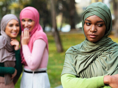 Unhappy woman standing alone as bad friends talk nearby