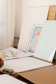 A young artist sitting on the floor surrounded by their artworks