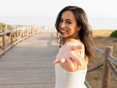 A smiling woman posing outdoors with one hand reaching upwards, symbolizing hope, faith, and the desire for personal growth